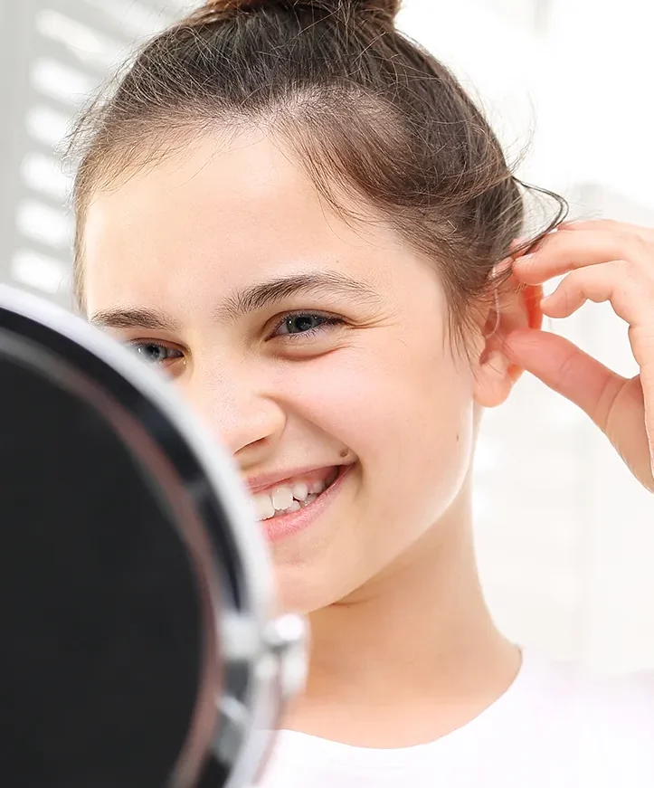 Happy girl fitting hearing aid in the mirror